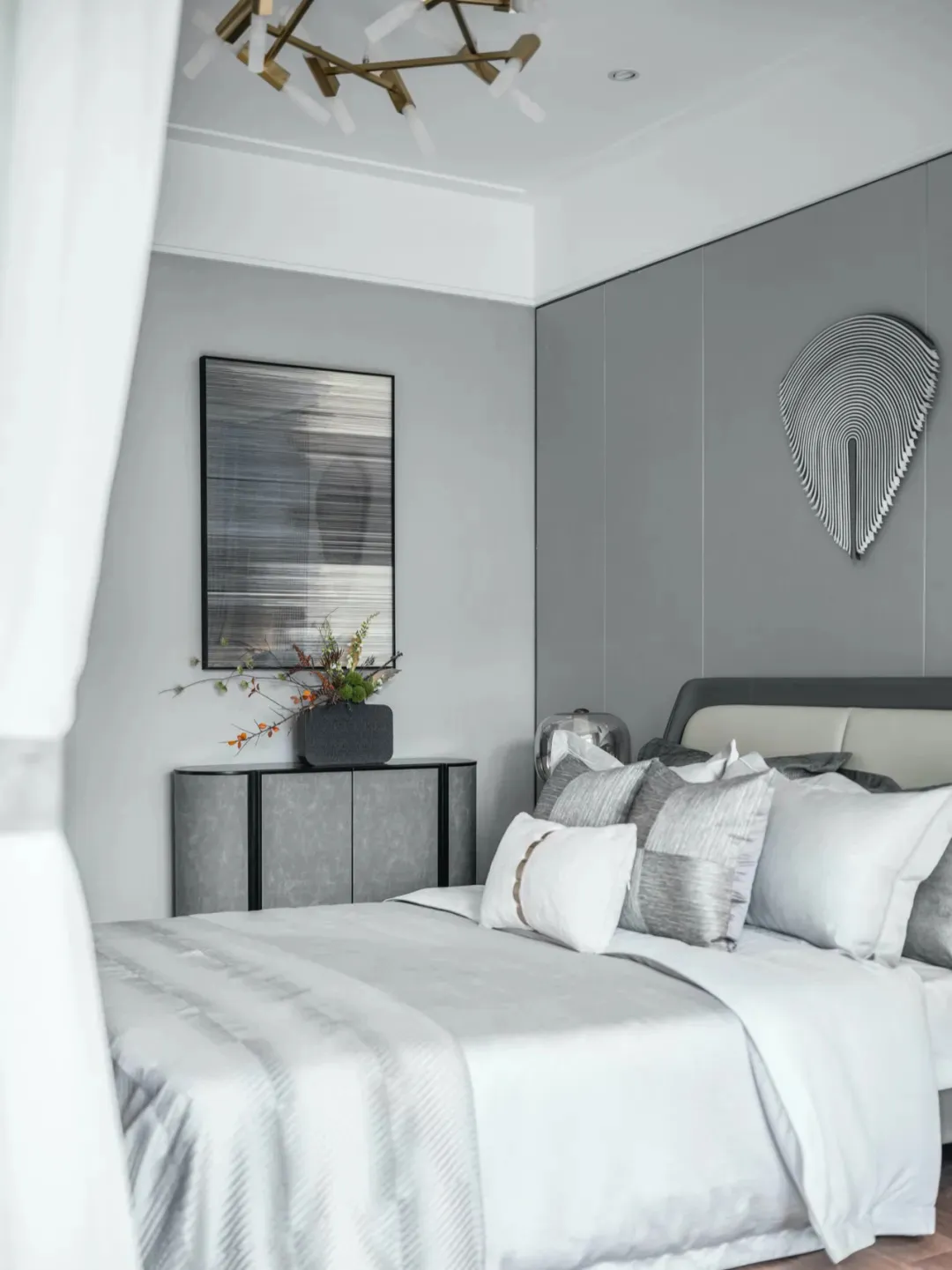 A modern minimalist bedroom with a grey bed, white bedding, and geometric art on the wall.