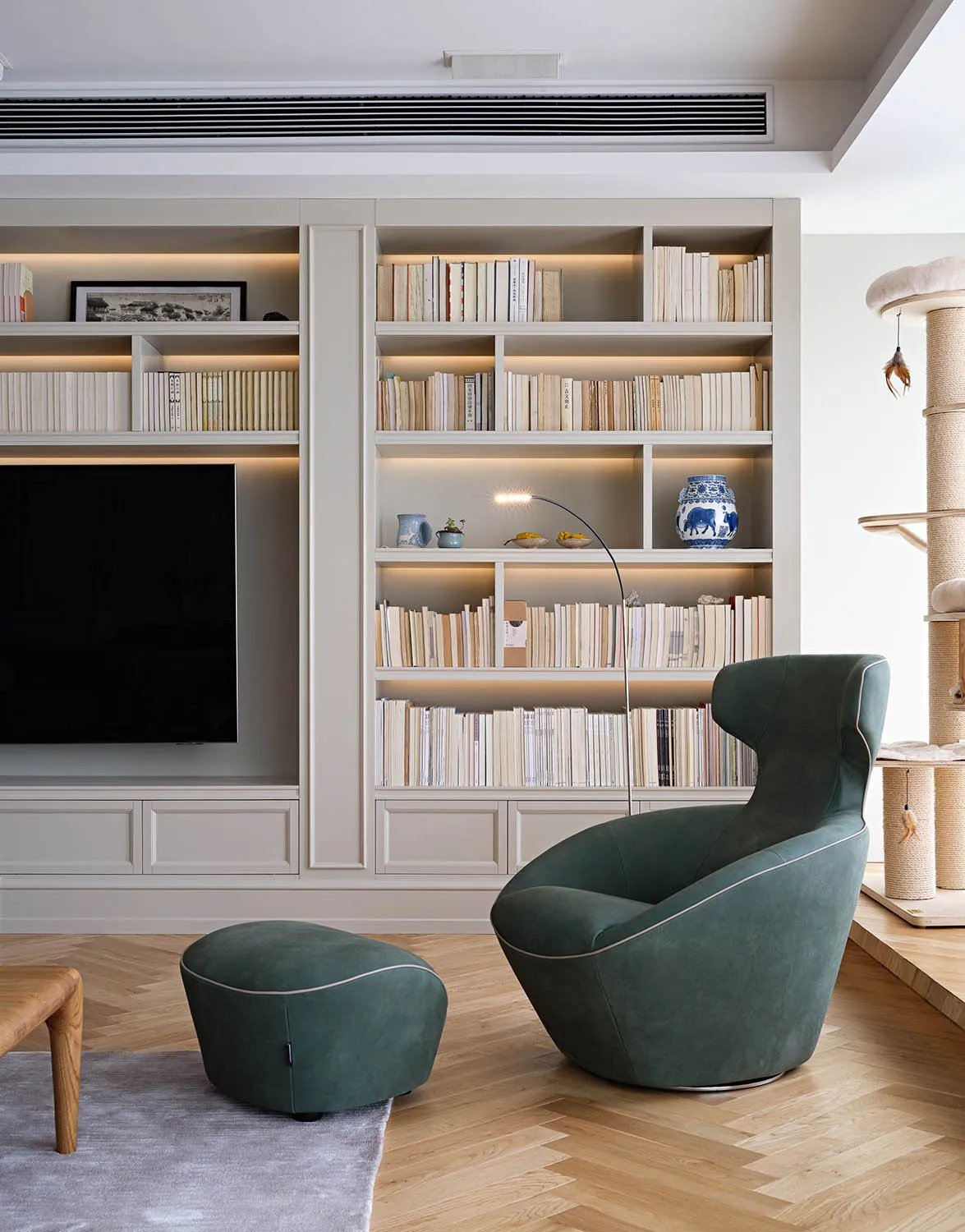 A modern minimalist living room with a green armchair, ottoman, and built-in bookshelves.