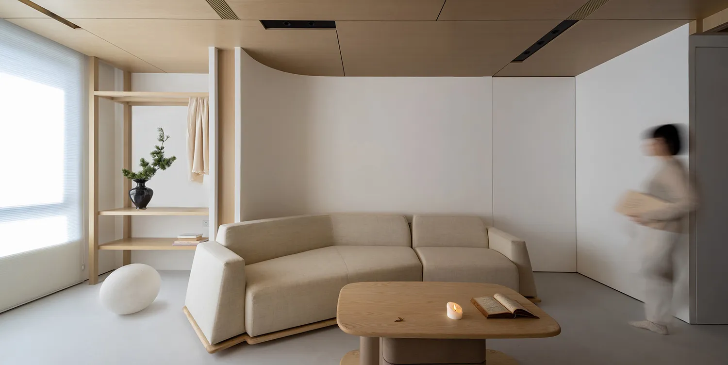 A modern living room with a neutral color palette, featuring a beige sofa, a wooden coffee table, and a minimalist design.