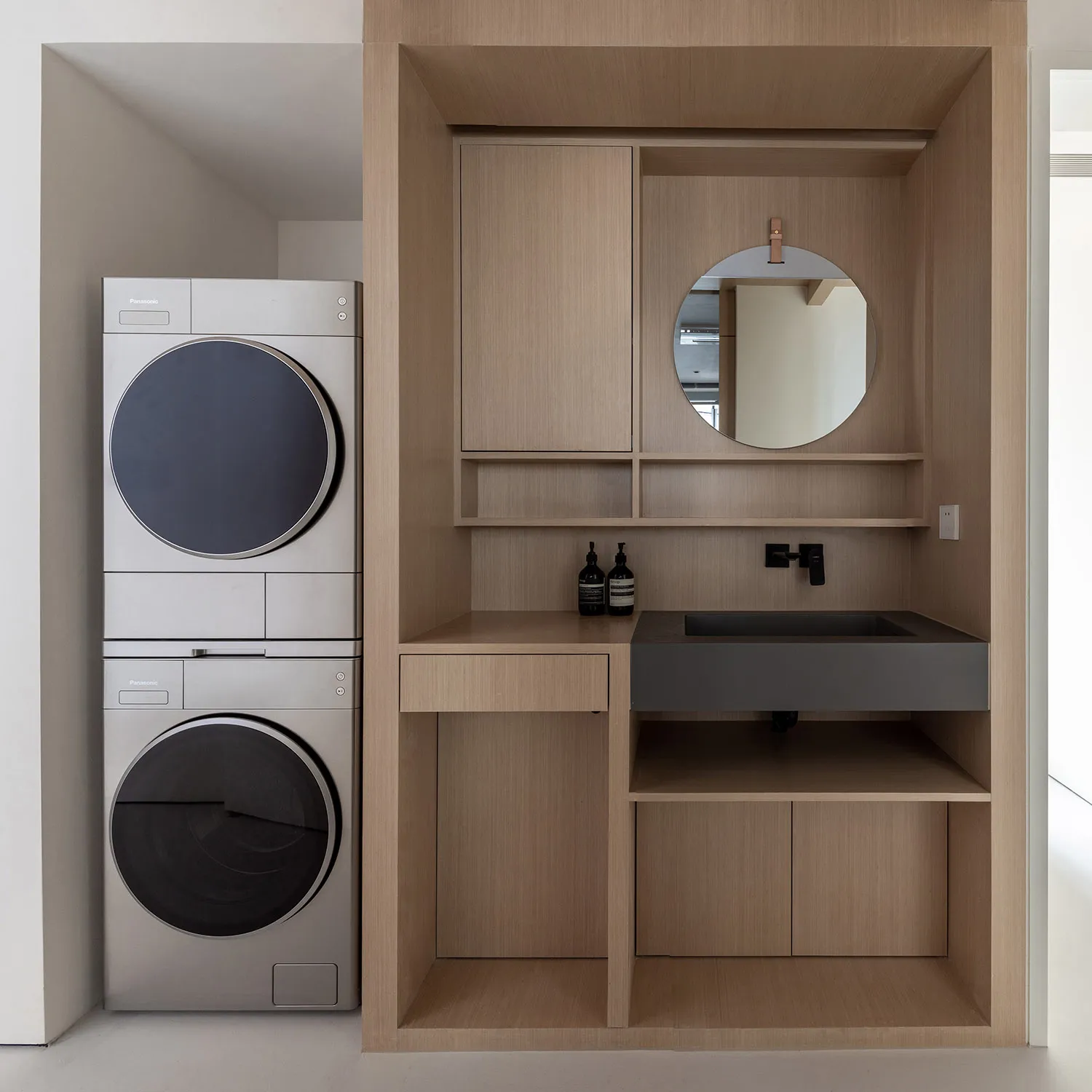 Modern minimalist laundry room featuring a stainless steel washer and dryer, integrated shelving, and a sleek black sink with