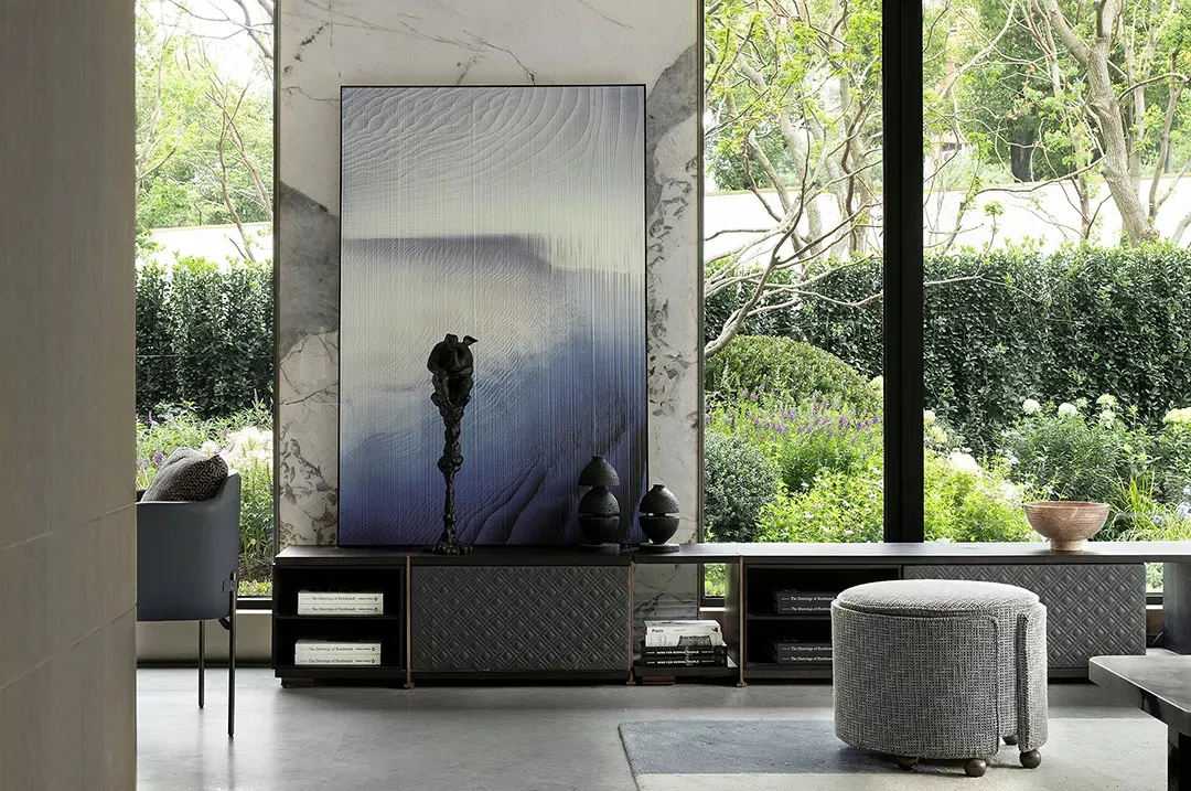 A modern living room featuring marble walls and furniture, with a large abstract art piece and a large window overlooking a g