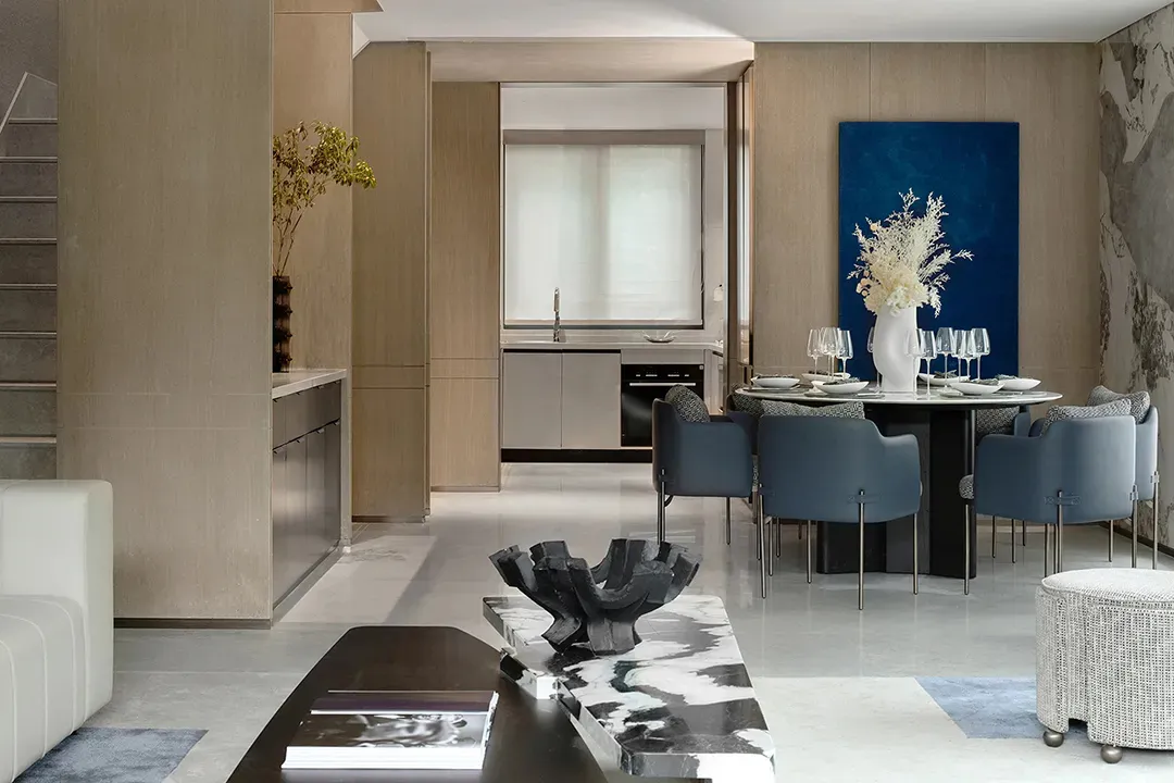 A modern residential dining space featuring a contemporary table with blue chairs, a marble coffee table, and a blue abstract