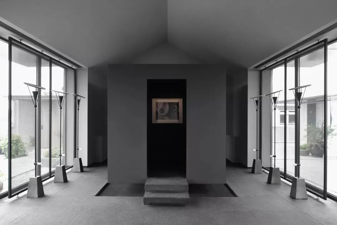 A minimalist art gallery showcases art pieces framed by concrete walls and large glass windows.