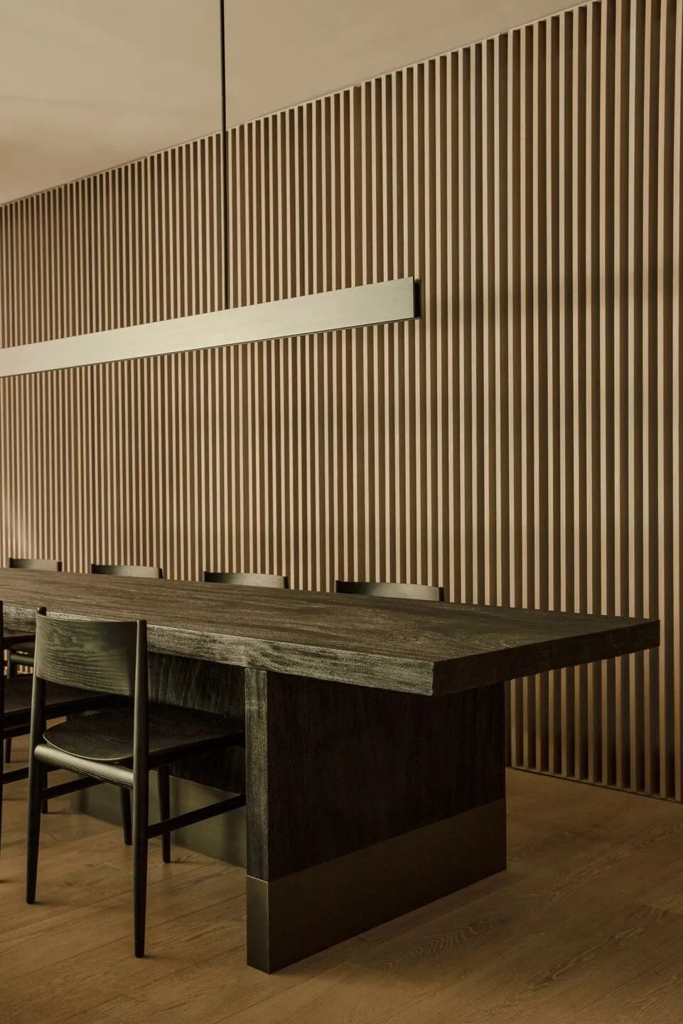 Modern minimalist restaurant interior featuring a wooden table and chairs against a wooden panel wall.