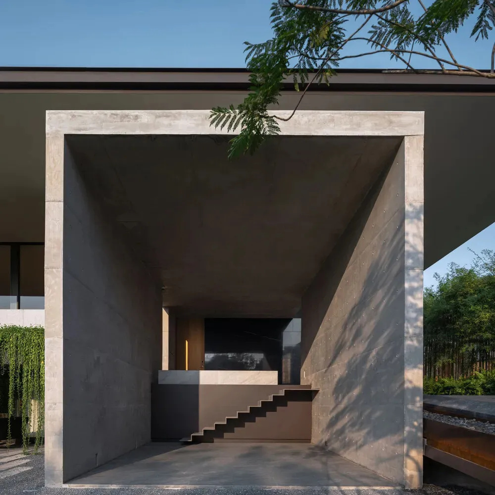 Concrete entrance lobby with stairs and greenery in the background.