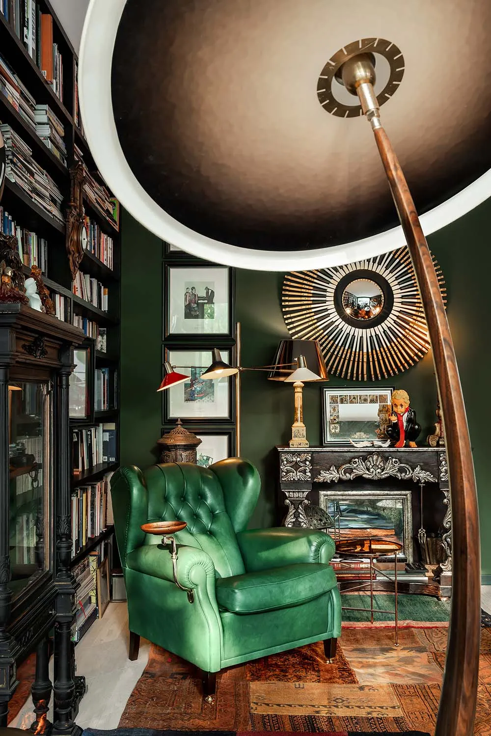 A modern home library featuring a green armchair, hardwood floors, and a large bookshelf filled with books.