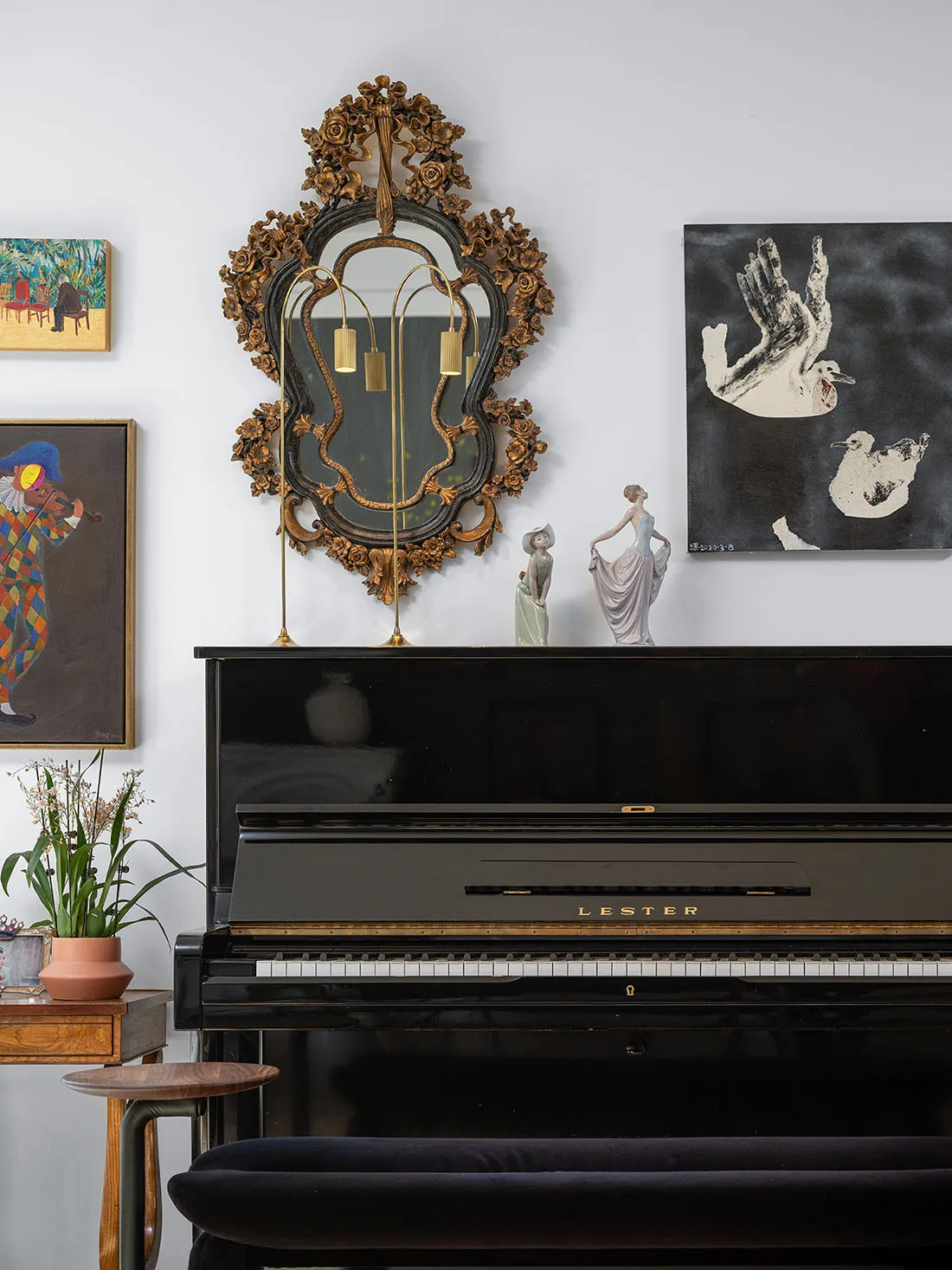 A black piano adorned with a framed mirror and sculptures, accompanied by framed artworks on the wall.