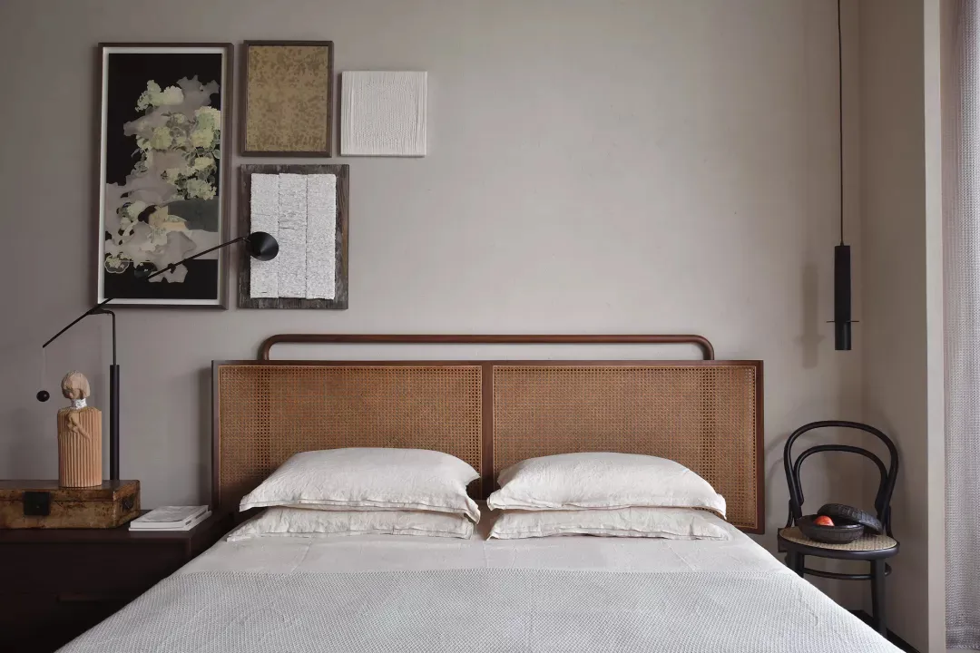 Minimalist bedroom with a wooden rattan headboard, white bedding, and a hanging black lamp.