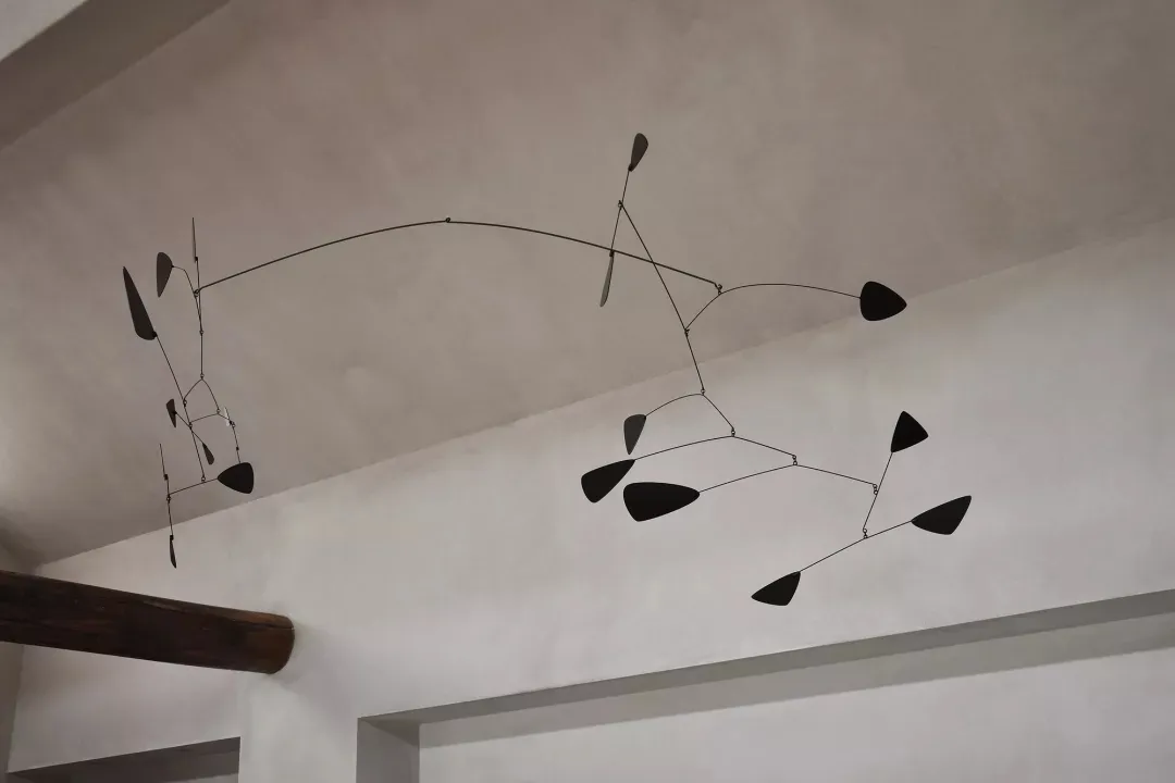 A minimalist metal abstract mobile sculpture consisting of geometric shapes arranged on a wire frame, hanging from the ceilin