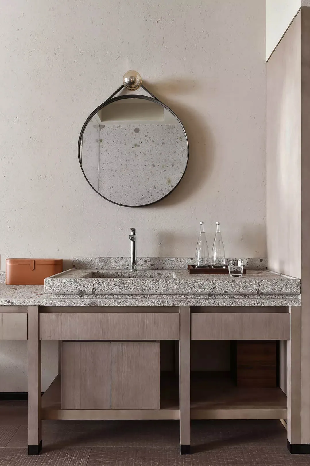 A modern bathroom with a concrete vanity including a sink, faucet, mirror, and storage underneath.