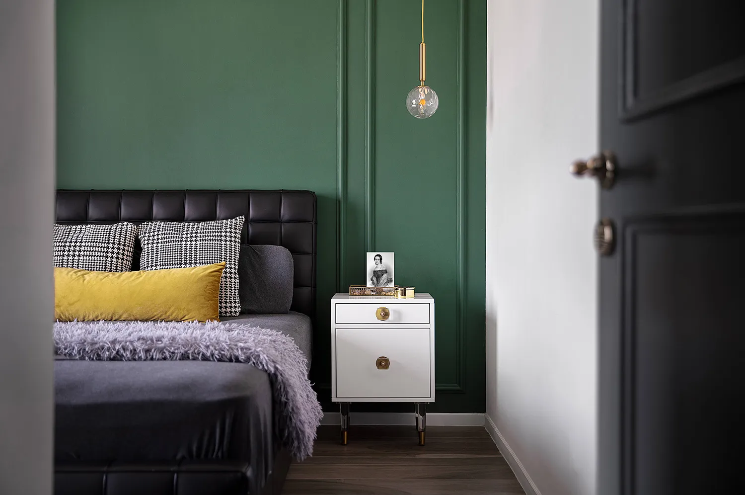 Modern bedroom with black leather headboard, yellow accent pillows, and a white nightstand with a spherical pendant light han
