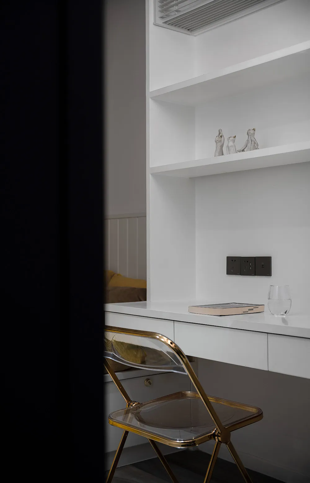 A modern home office with a clear folding chair, matte white wall, and minimalist decor.