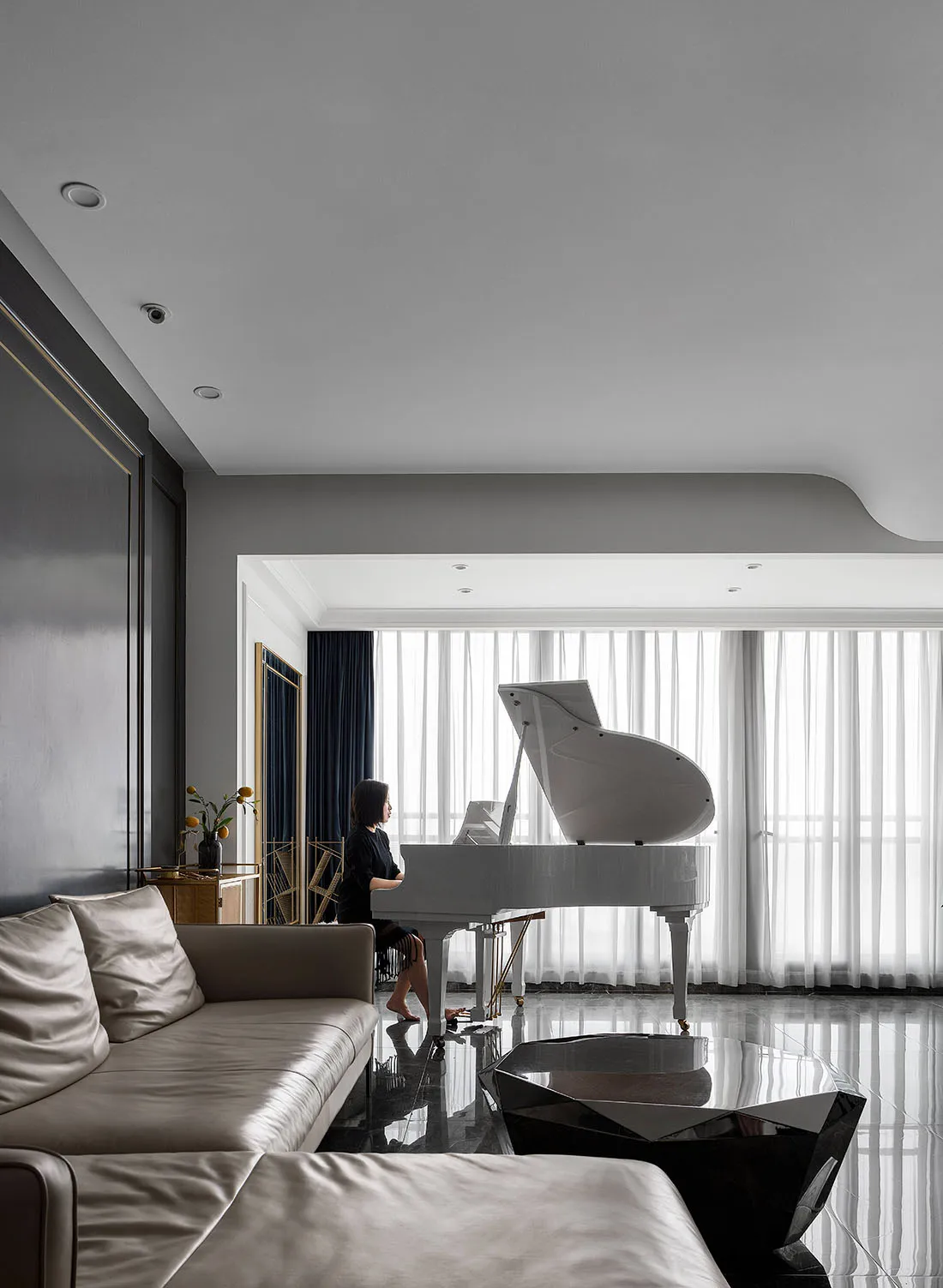 A modern living room with gray tiles, white curtains, and a leather couch featuring a grand piano.