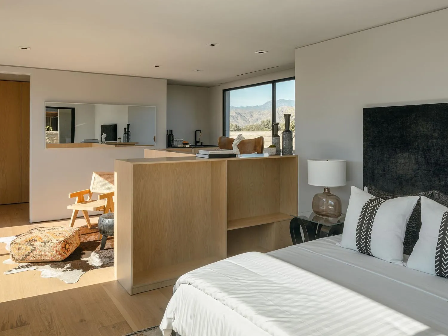 A modern bedroom with a wooden bed frame, white bedding, and a wooden desk with built-in shelves.