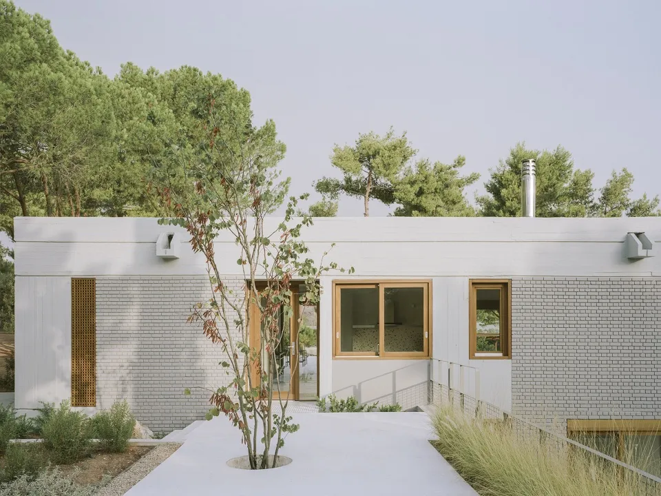 A modern house with white brick walls and large windows surrounded by greenery.