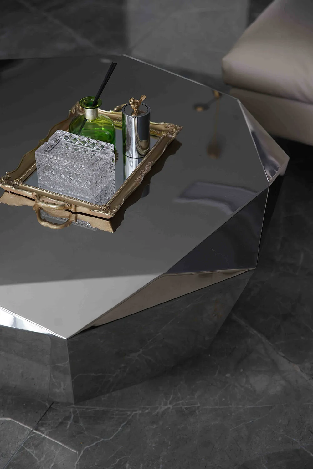 A modern metallic coffee table with a geometric design and a tray of decorative items on top.