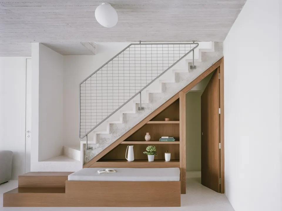 A minimalist house features a concrete staircase with a white railing and a wooden bench seat.