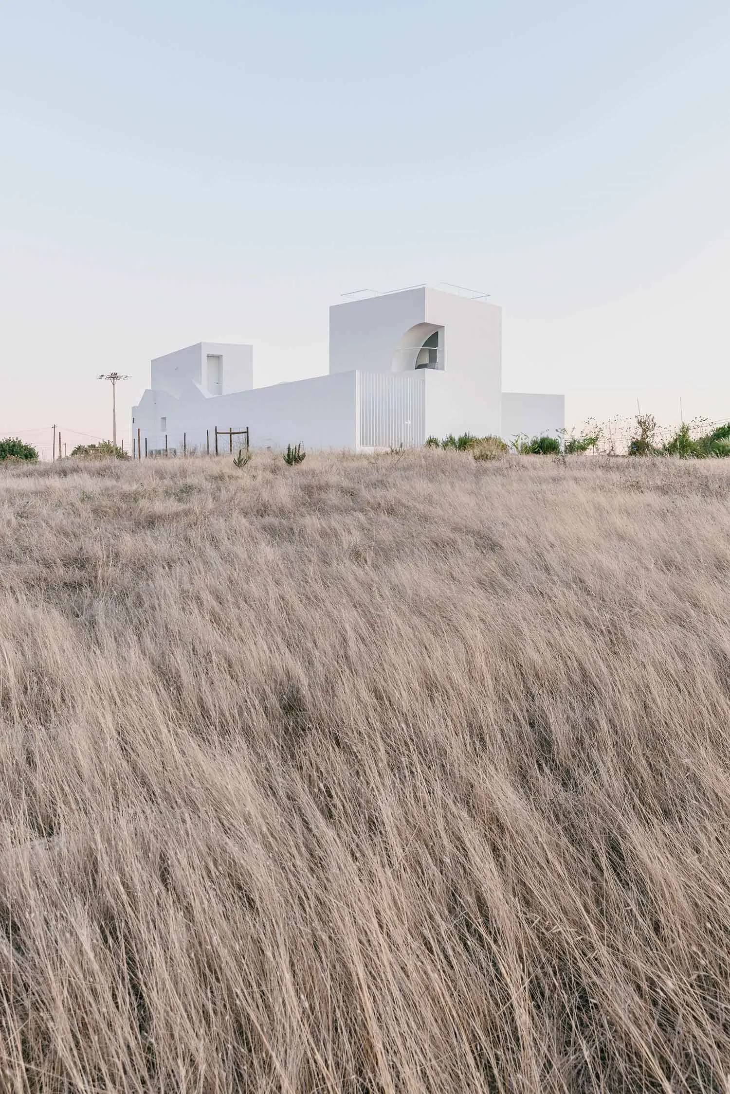A minimalist white house surrounded by dry grass in a canyon landscape.