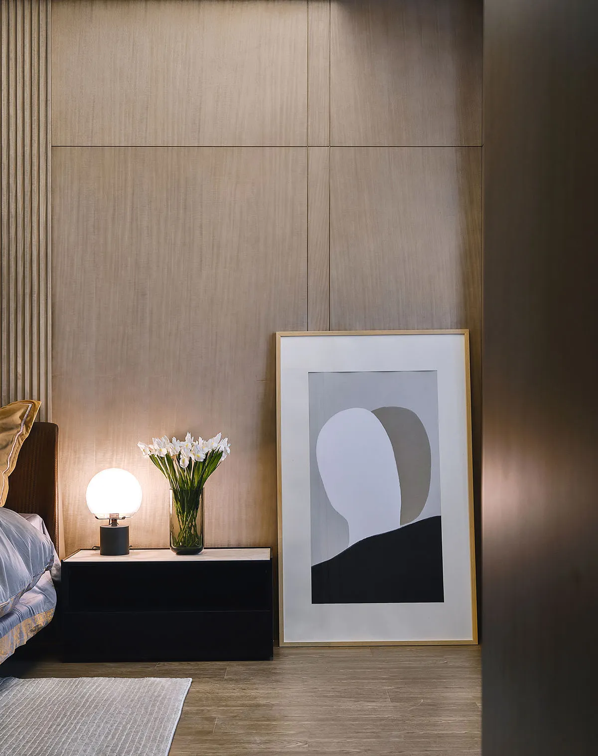 A modern bedroom featuring a wooden textured wall and a bedside table with a spherical lamp and a vase with white flowers.
