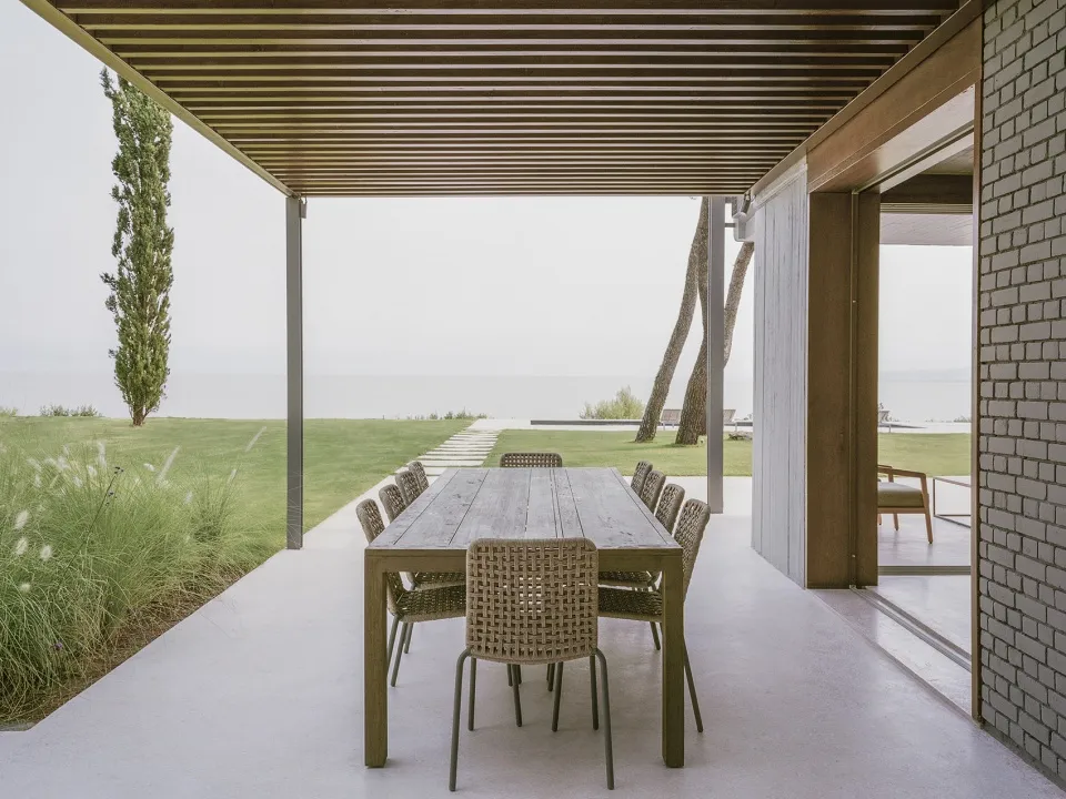Outdoor dining area featuring a wooden table and rattan chairs with a sea view.
