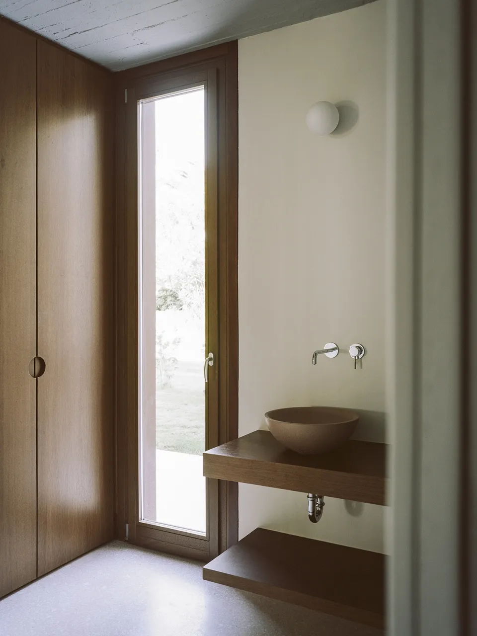 A minimalist bathroom with wooden elements, featuring a small sink and a large window.