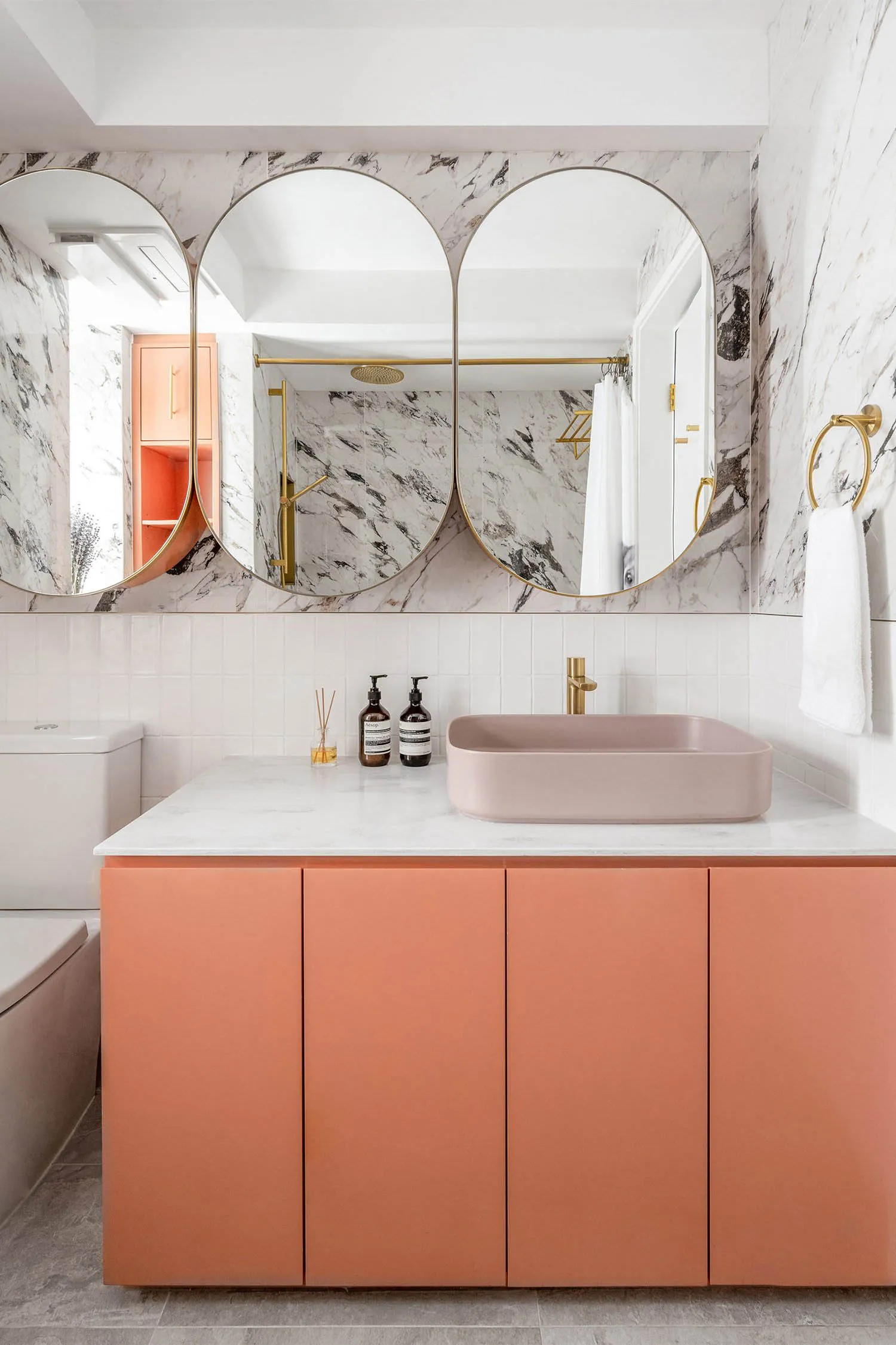 Modern bathroom with marble walls, concrete flooring, pink cabinets, and pink sink.