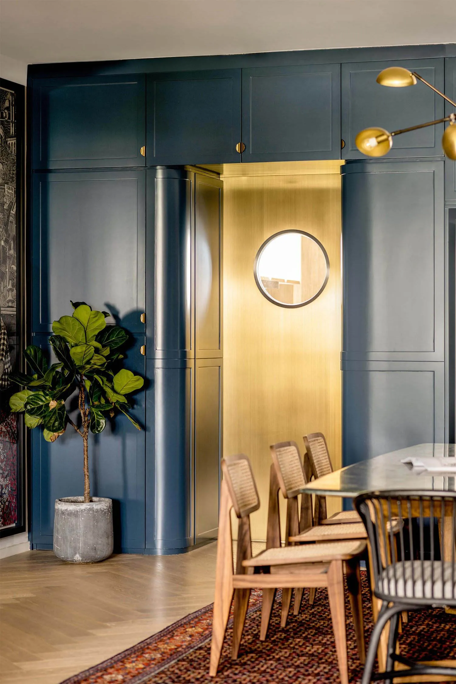 A modern dining room with blue cabinets and a brass door with a circular window.