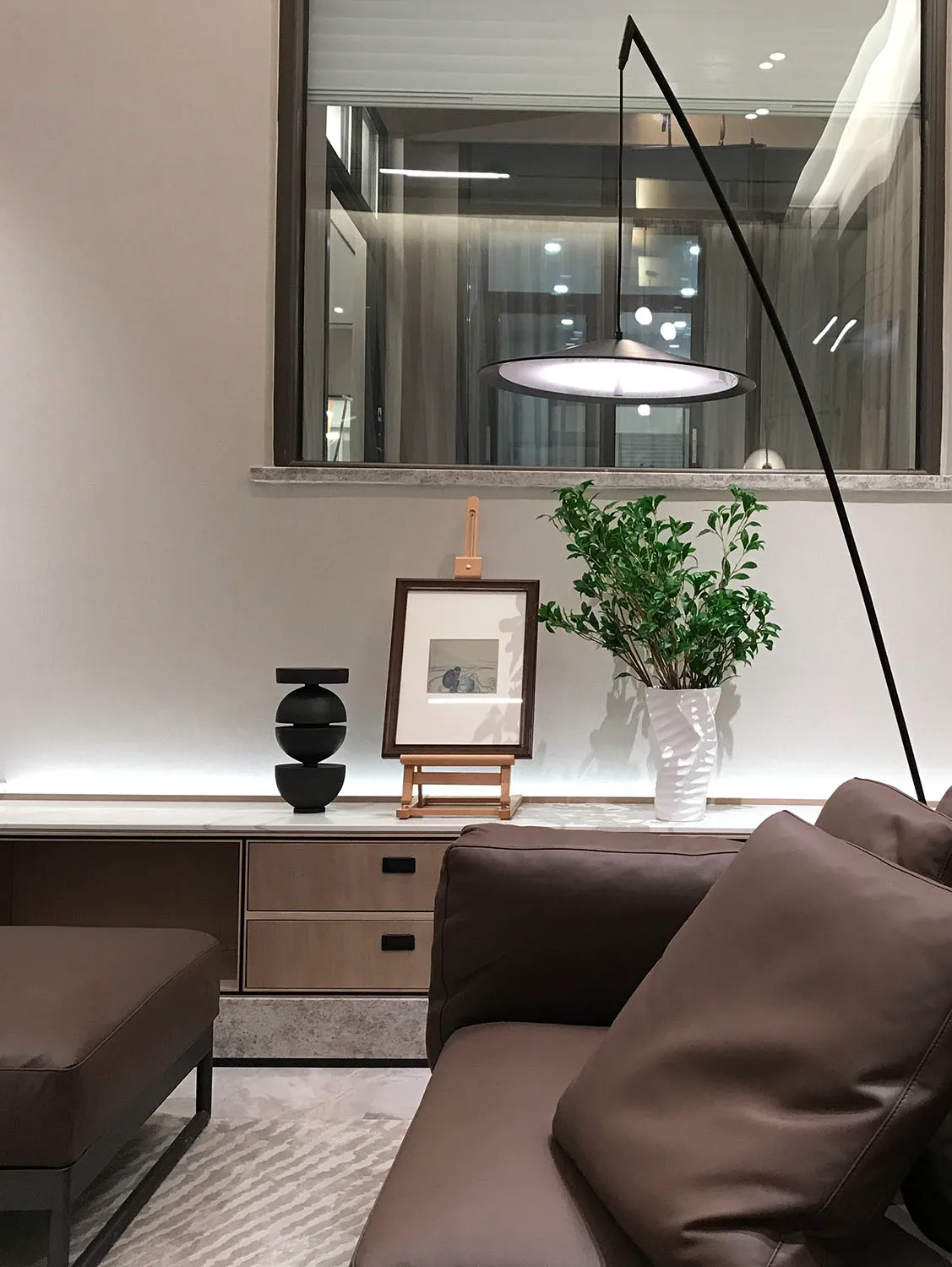 現代客廳內擺放棕色皮革沙發、吊燈，以及木質層架上的植物。