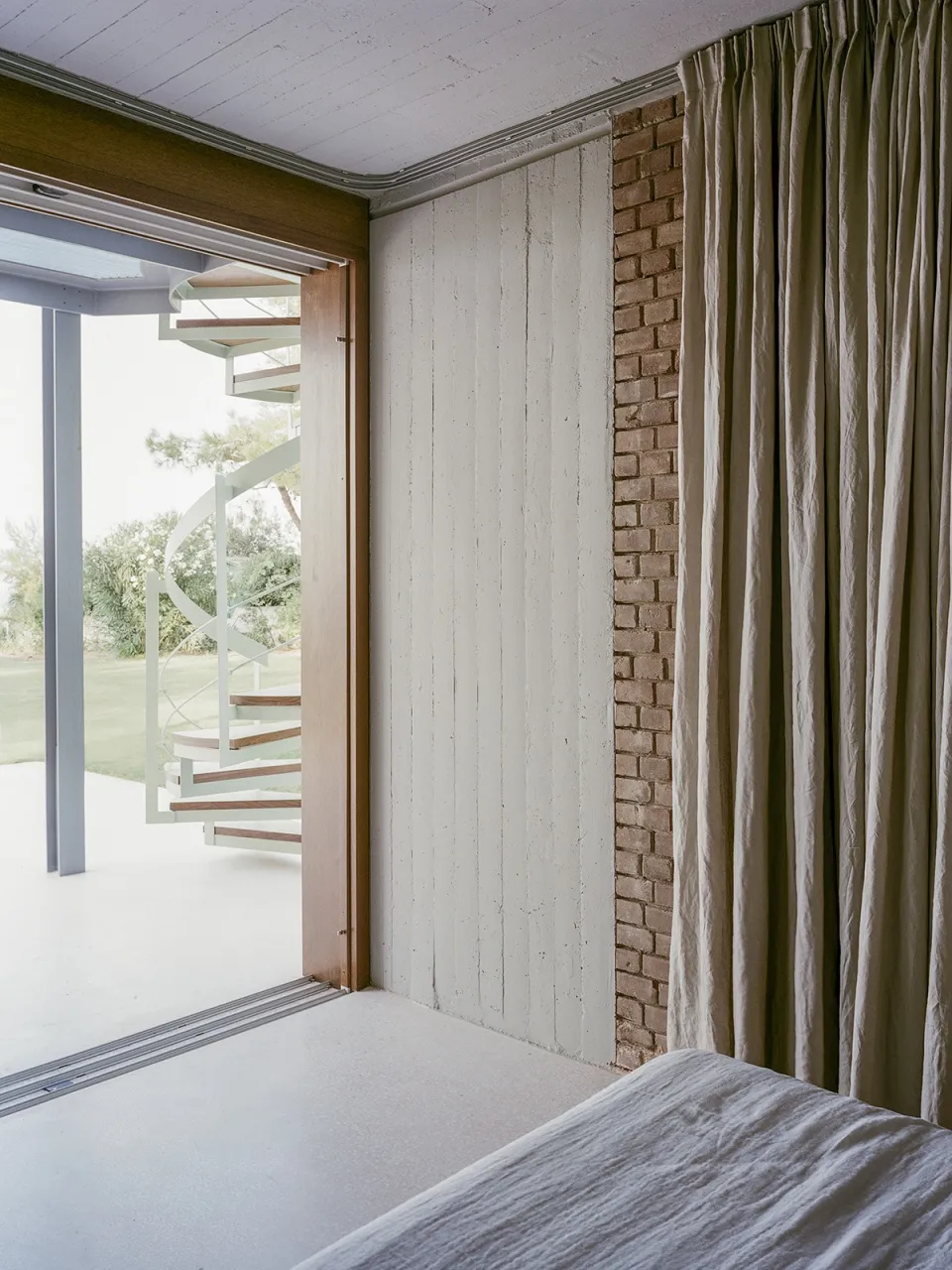 Minimalist bedroom featuring white curtains, wood paneling, and concrete elements.