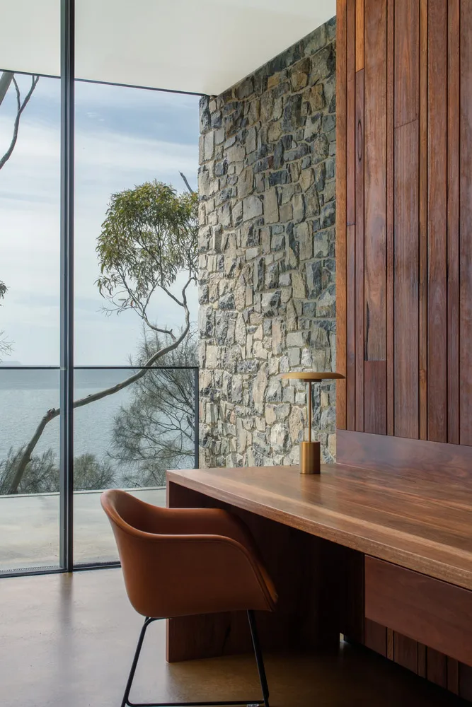 A modern home office with a stone wall, wooden desk, and leather chair.