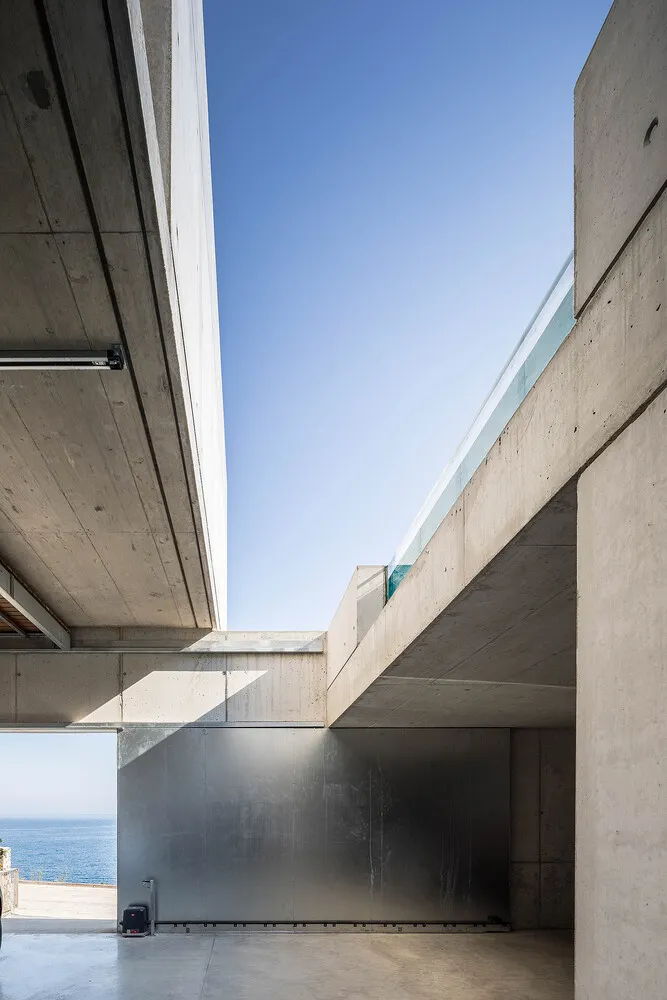 A modern house with a concrete facade and glass balcony overlooking the ocean.