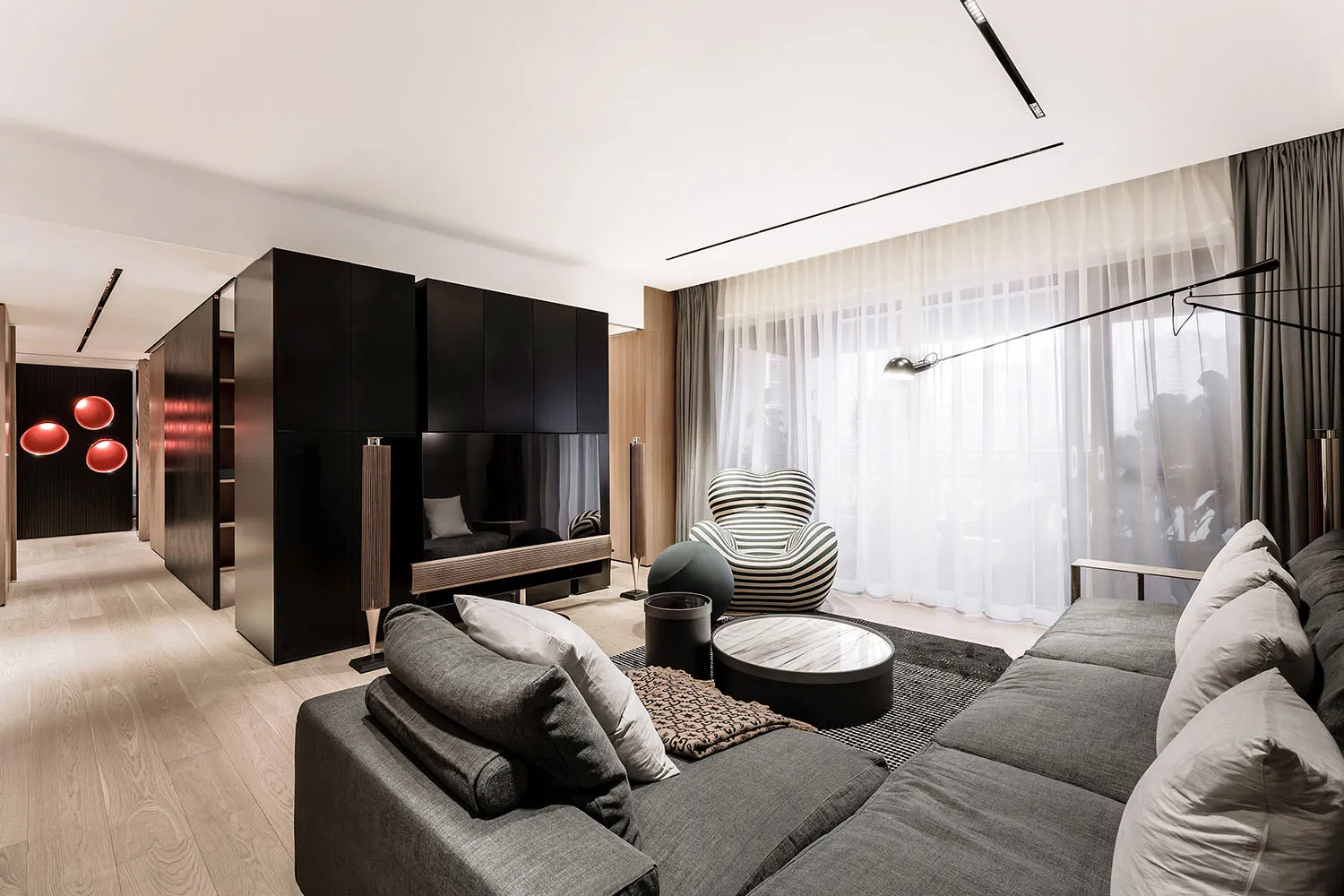 A modern minimalist living room with a dark accent wall, large windows, and a gray sofa.