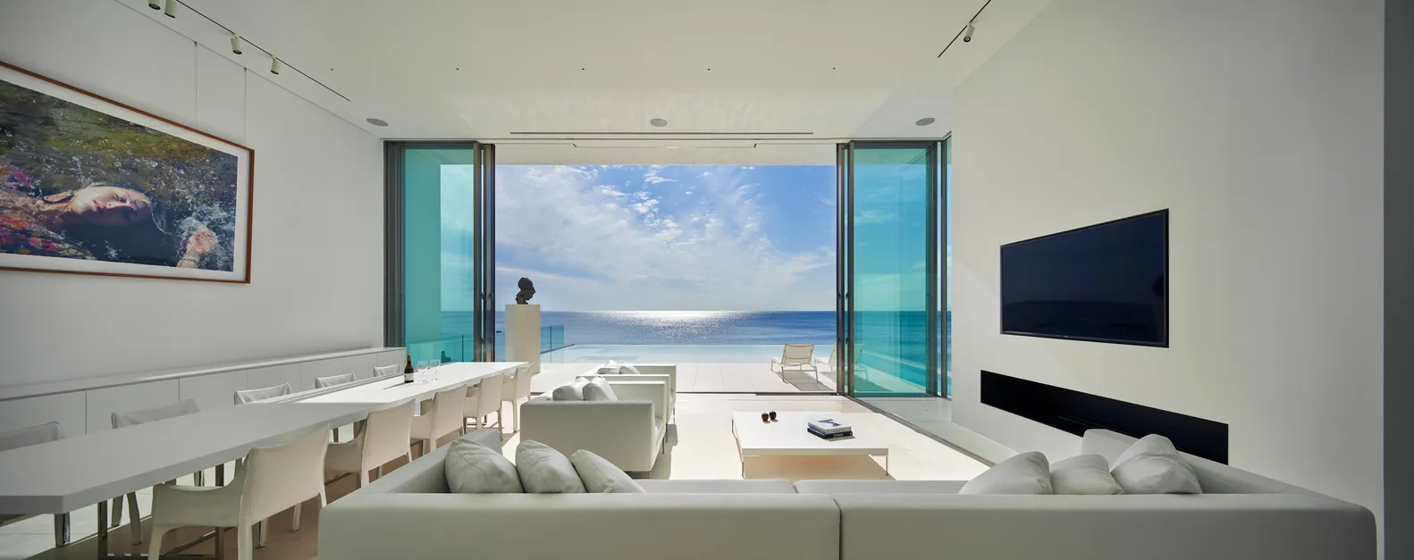 A modern living room featuring clear glass doors that open to reveal an ocean view.