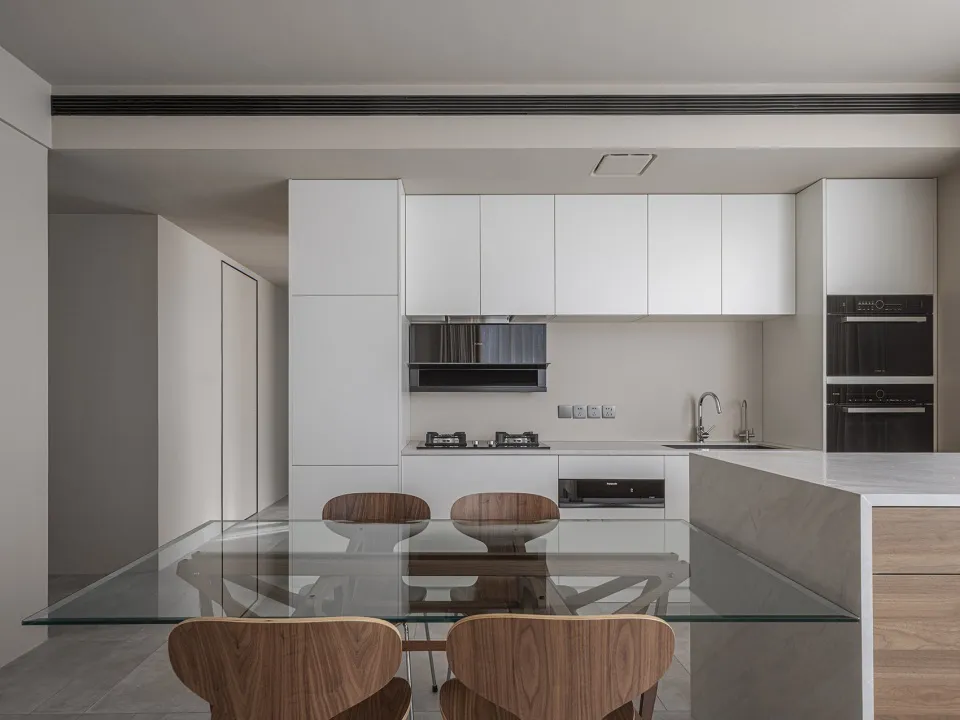 Modern kitchen with white cabinets, concrete countertops, wooden furniture, and a glass table top.
