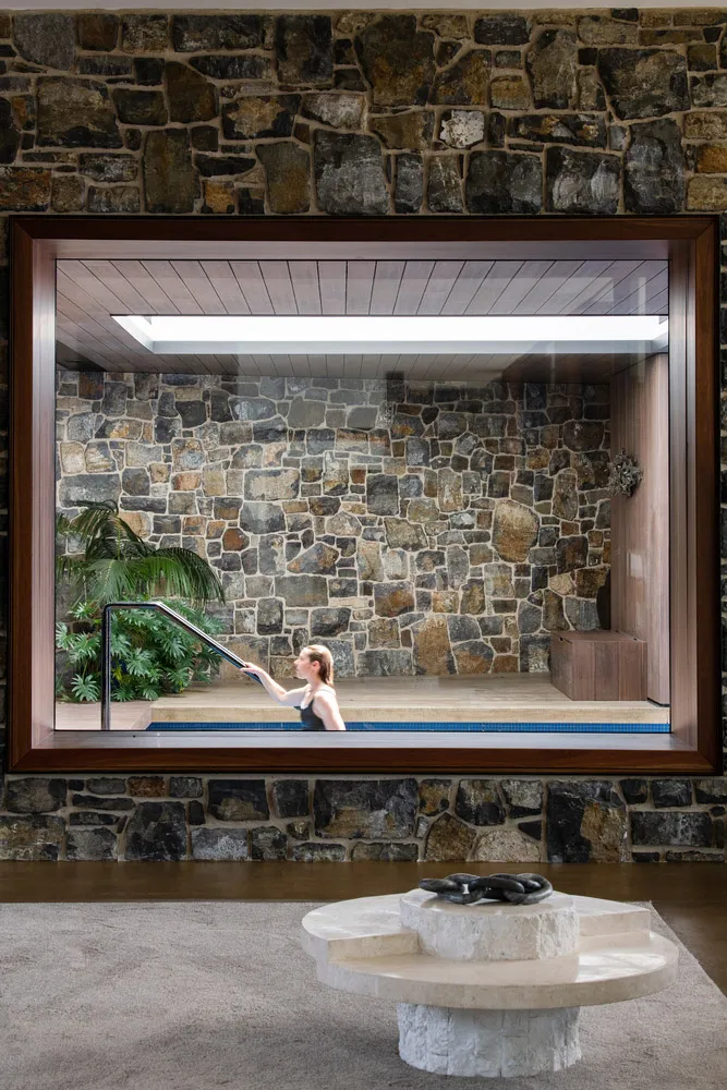 A modern living space featuring stone walls and a glass enclosure with a woman in a pool.