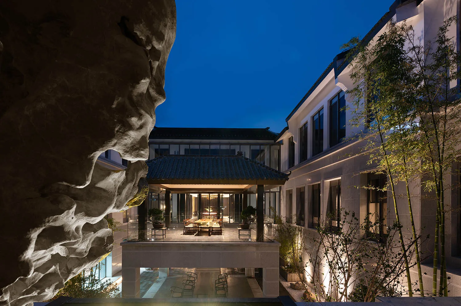 An outdoor space at night with concrete walls, a glass pavilion, and plants.