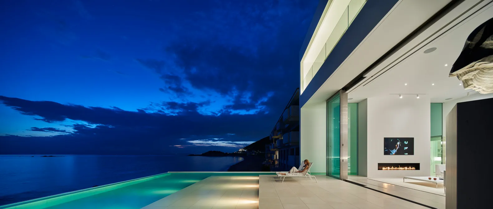 Modern residential exterior featuring glass and concrete at night with ocean view.