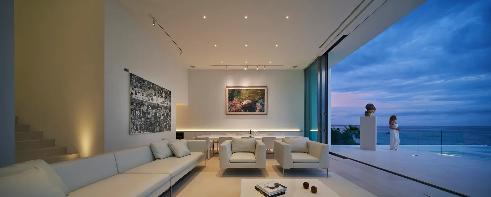 A modern residential interior with white furniture and glass walls.