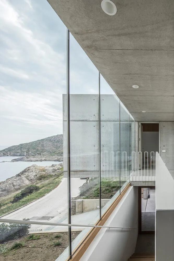 Modern residential interior featuring glass and concrete materials, overlooking a coastal landscape.