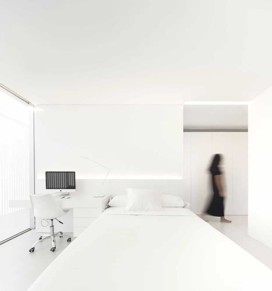 A minimalist bedroom with a white bed and desk.