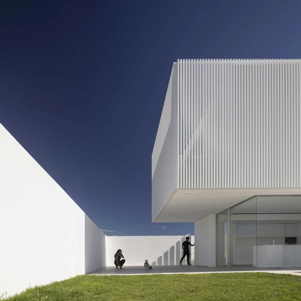 Modern house with a minimalist design featuring a white exterior clad with white ribbed panels.