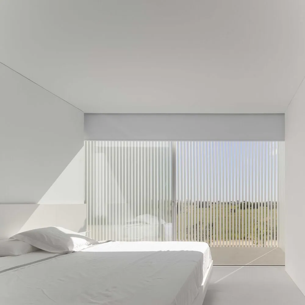 A minimalist bedroom with a white bed and wooden blinds.