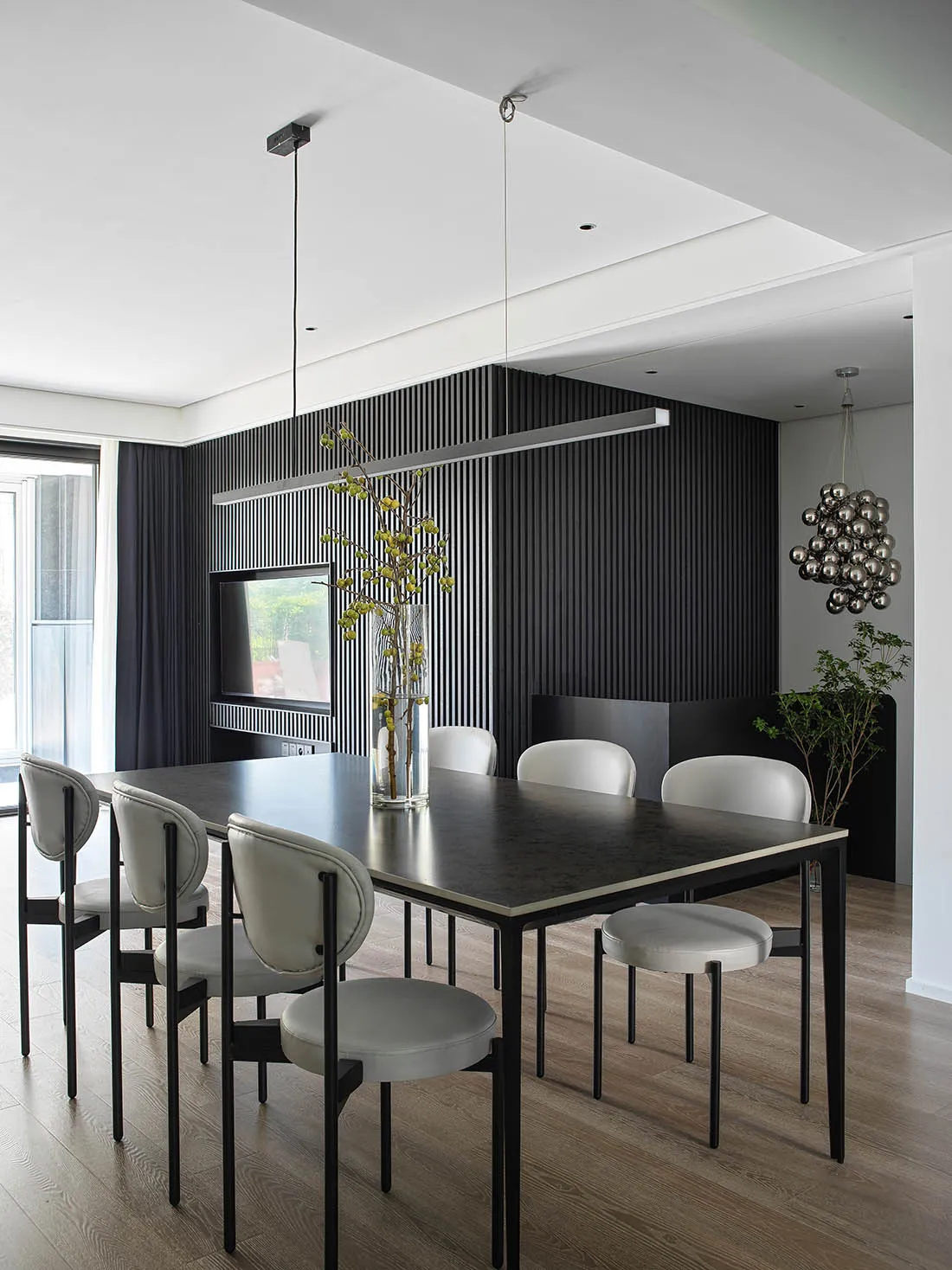 A modern dining room featuring a black metallic pendant light, white leather chairs, and a wooden dining table.