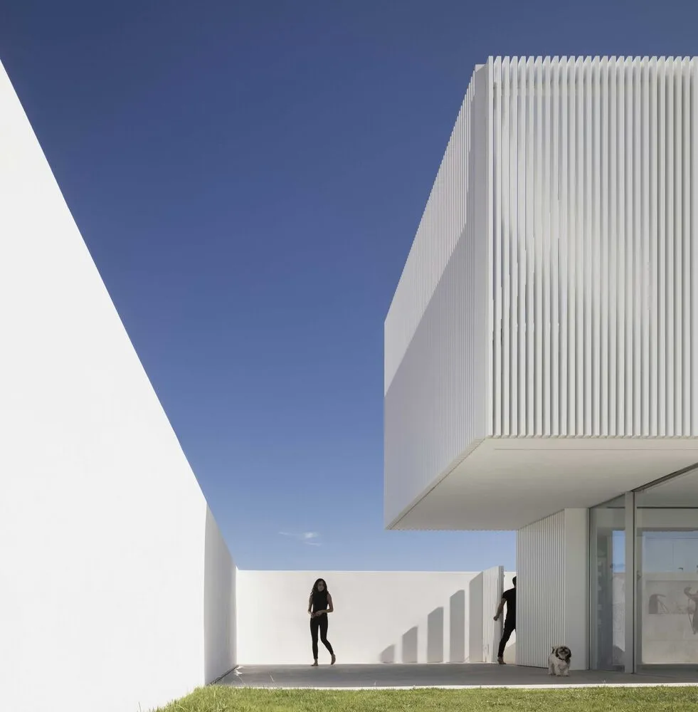 A modern residential exterior featuring white concrete walls under a clear blue sky.