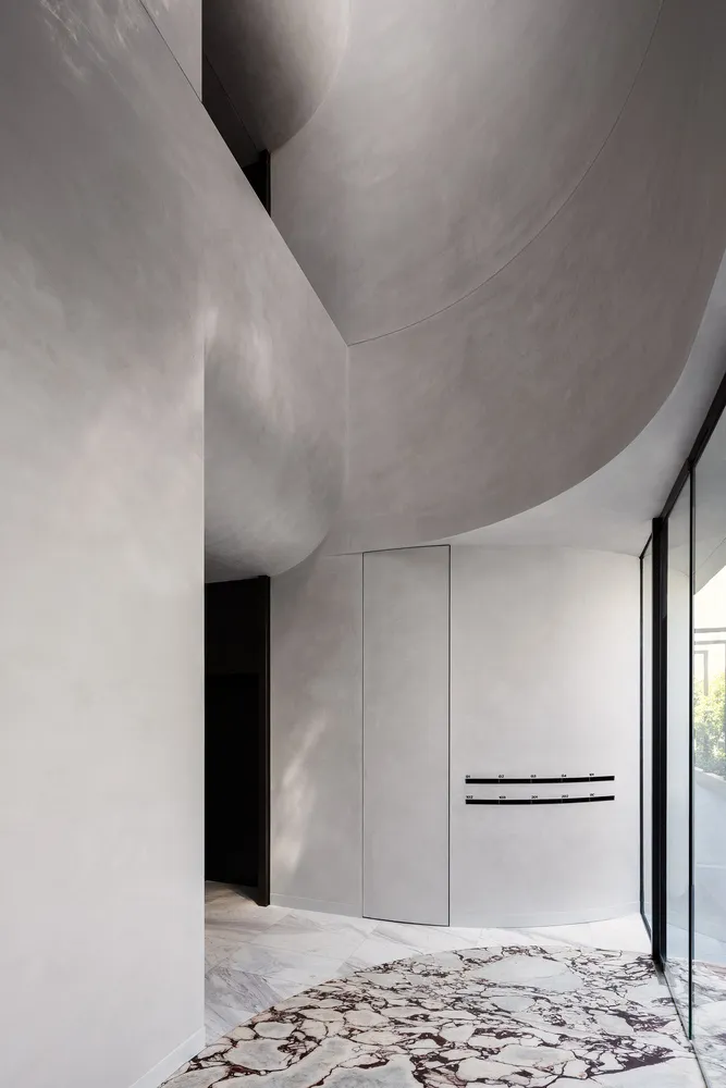 A minimalist space featuring concrete walls and a marble floor, with a curved ceiling and spacious layout.