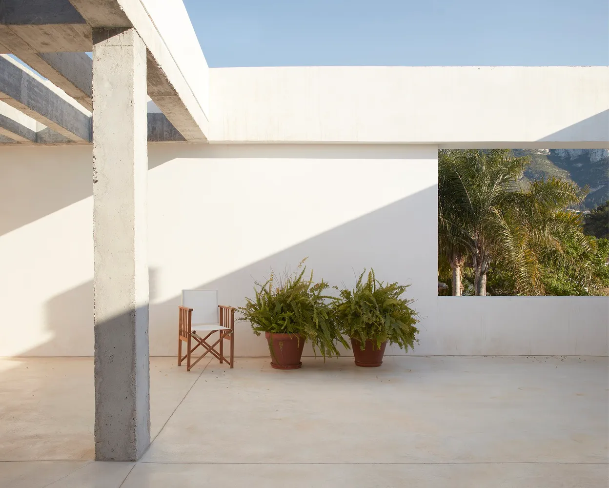 White minimalist patio with concrete planter pots and lush green plants, featuring a simple concrete structure and a clear sk