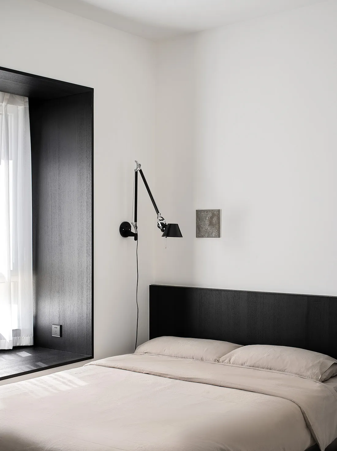 A modern bedroom with a minimalist design featuring black and white tones, a black headboard, beige bedding, and a wall-mount