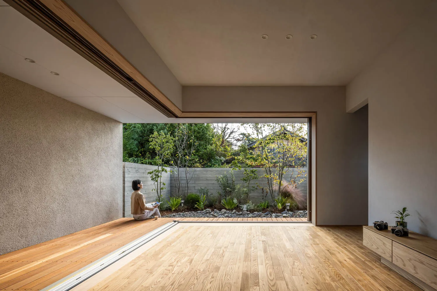 A modern interior space featuring a wooden floor and a garden view through a large window.