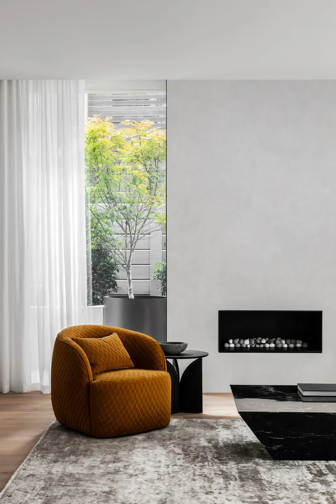 A modern living room with a minimalist design featuring a mustard-colored chair, a black marble coffee table, and a large win