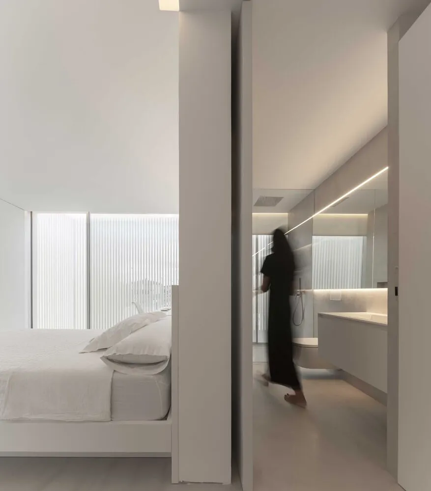 A minimalist bedroom with concrete flooring, glass windows, and white furniture.